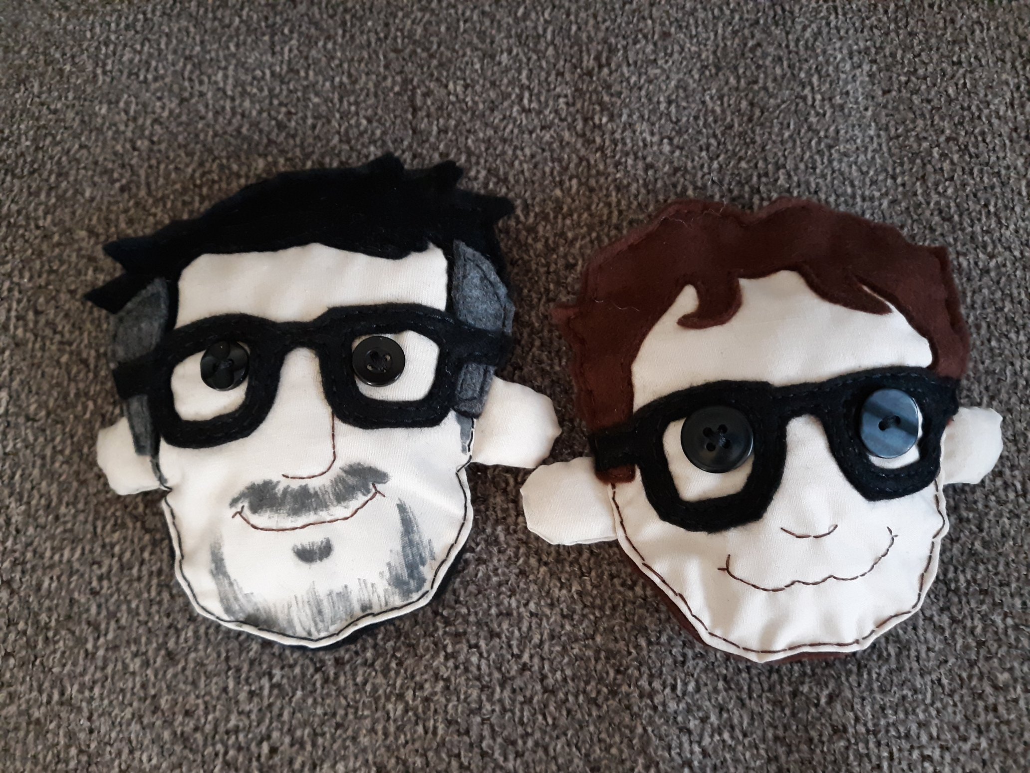 Two pins of the heads of John Flansburgh and John Linnell laying down on a couch. Their hair and glasses are made of felt, their skin is made of polyester cotton, and their eyes are black buttons. Their noses and mouths were embroidered on. Flansburgh's facial hair was drawn on with a fabric marker.