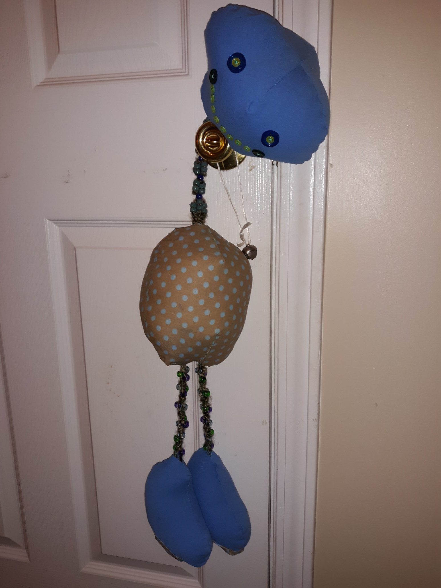 The same doll hanging off of a doorknob to show off the beaded neck and the beaded legs.