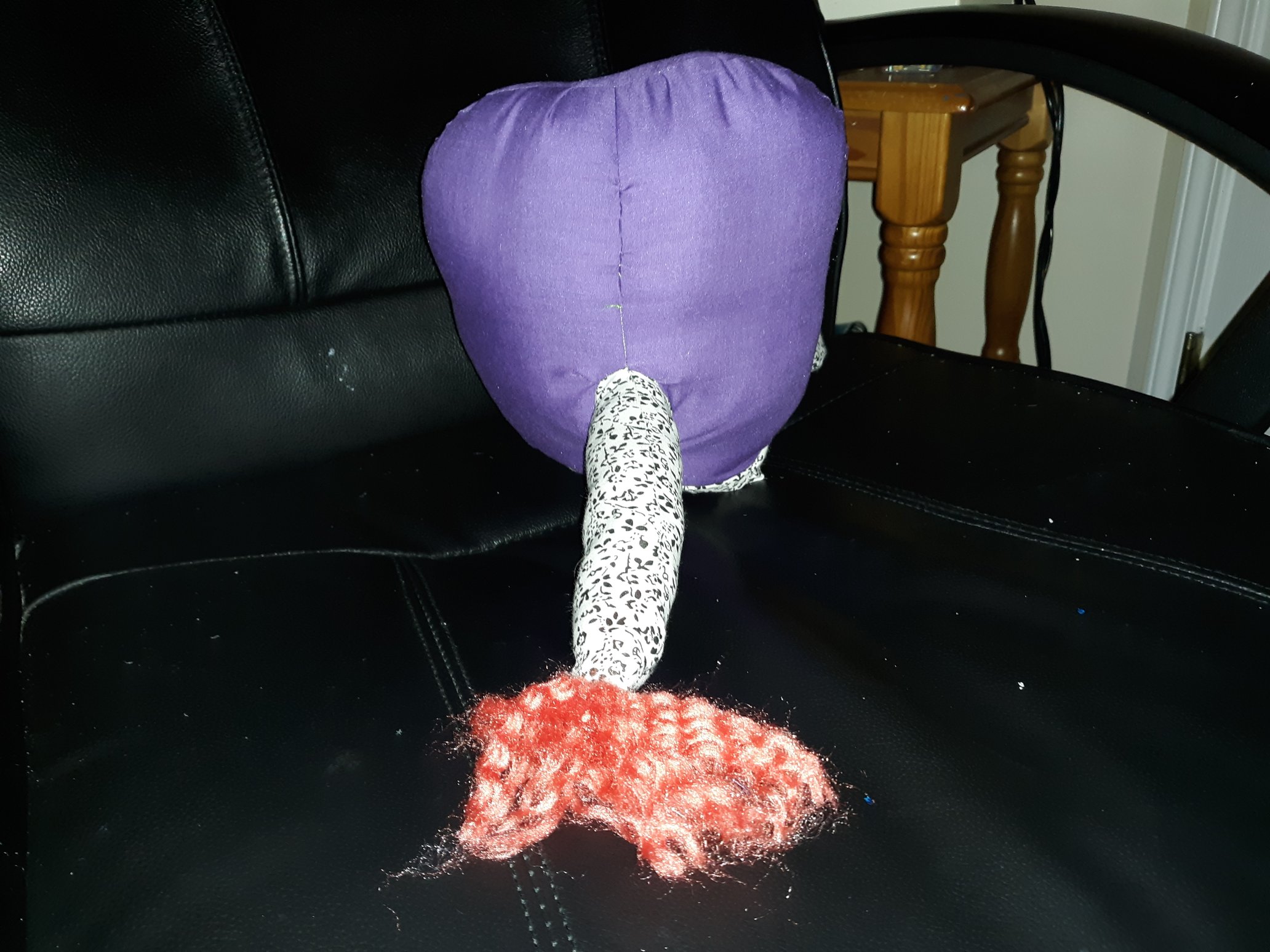 The back of the doll. There is a tail coming out with a salmon colored puff of yarn at the end of it. The tail is of the same black and white floral pattern as the legs.