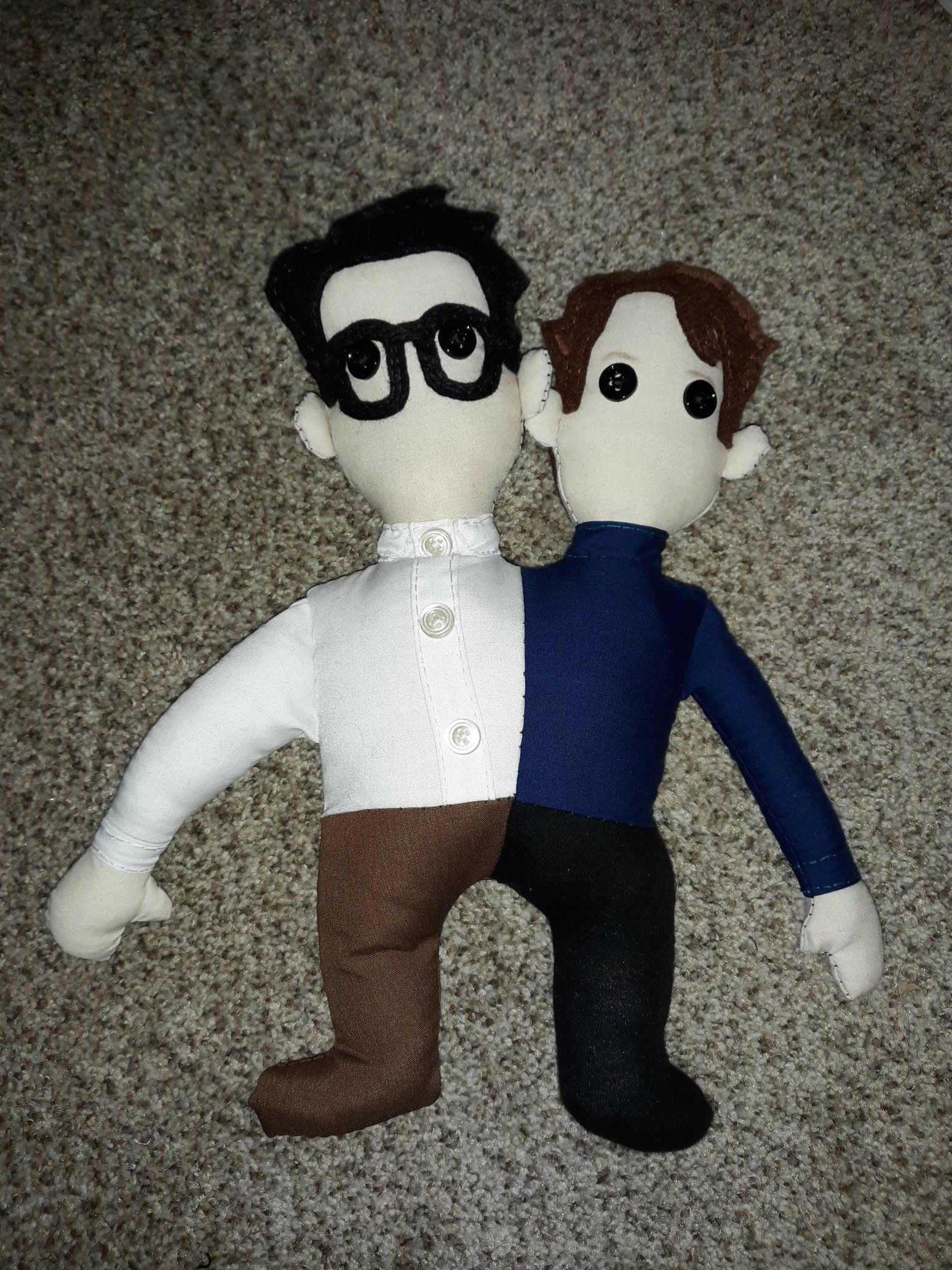 The two headed Johnster. It looks the same as the one above, but a bit more refined. Half of a young John Flansburgh has been sewn to half of a young John Linnell. Flansburgh is on the left and Linnell is on the right. Flansburgh is wearing a white button up shirt with brown pants. Linnell is wearing a dark blue turtleneck with black pants. They both have black button eyes. Flansburgh is wearing black glasses.