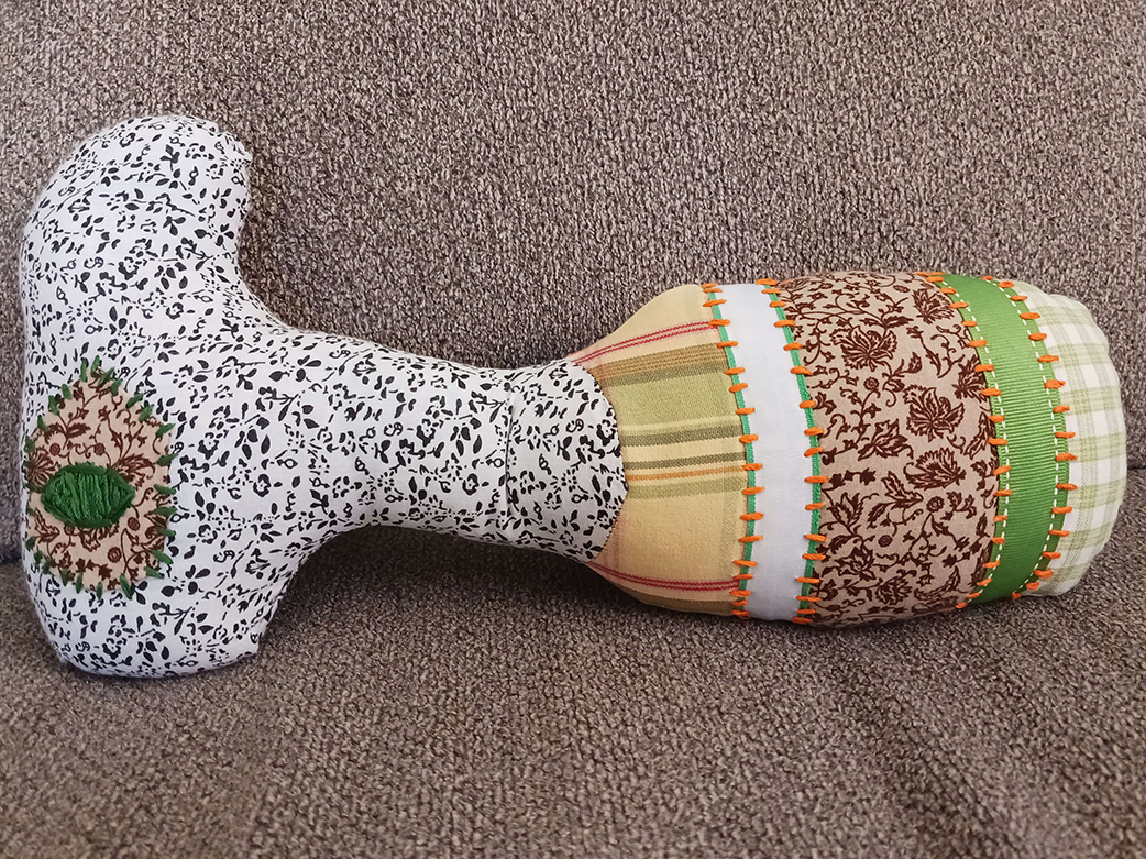 A doll laying on a couch. They have an oval head with a long neck and oval body. They have one large eye on the head.