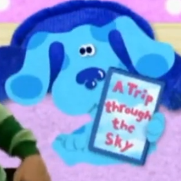 Blue is holding a book titled 'A Trip Through the Sky.' The cover is of a blue sky with clouds and has the title in red over it.