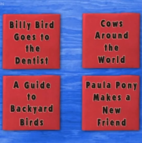 Four red books lay on top of a blue table. The first book has the title 'Billy Bird Goes to the Dentist.' The second book has the title 'Cows Around the World.' The third book is titled 'A Guide to Backyard Birds' and the fourth one is titled 'Paula Pony Makes a New Friend.'
