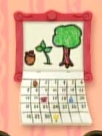A calendar is hanging on the wall with a salmon colored frame. The top half has a picture of an acorn, sapling, and a tree all next to each other. The bottom half of the calendar has all of the dates on it.
