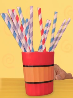 A red and orange cup sitting on top of a wooden counter. There are multiple straws coming out of it.