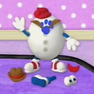 A toy egg is standing on top of a desk. It is wearing a hat and has arms, legs, and eyebrows that have a blue paw print stuck to them. There is a hat, leg, eyeballs, and a mouth laying down in front of the toy egg.