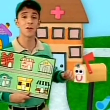Steve is holding a map of the neighborhood and has an orange hospital and with an orange mailbox behind him.