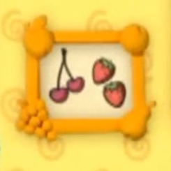 A yellow square frame hangs on the wall. The frame has different fruit in each corner. One corner is an apple, one corner is an orange, one is a pear, and another is a bundle of grapes. The picture inside the frame is of cherries and strawberries.