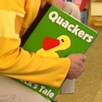Joe is holding a book that says 'Quackers: A Duck's Tale' on it. The book is green with an image of a yellow duck on it.