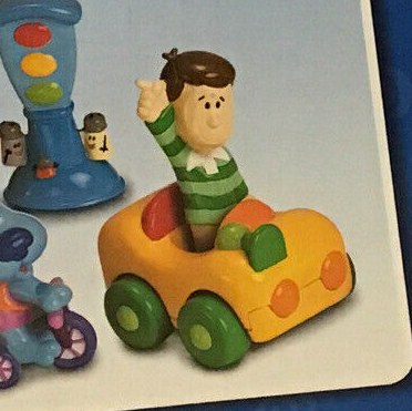 A toy of Steve standing inside of a toy car. The car is yellow with green wheels and a green horn.