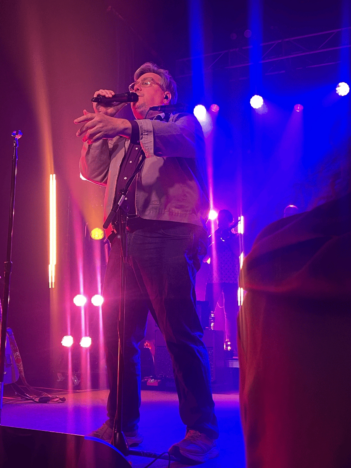 John Flansburgh on stage singing into a microphone.