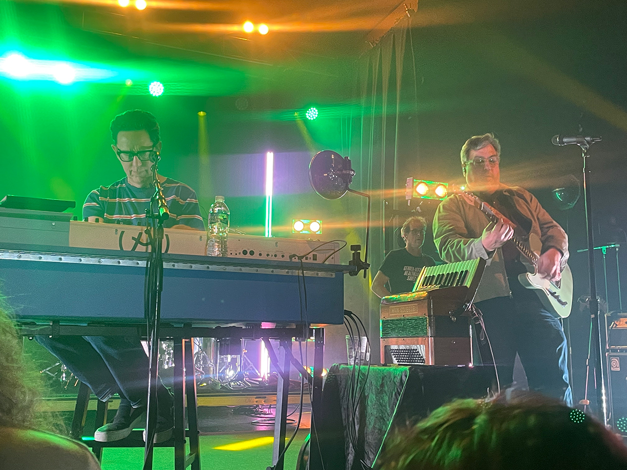 John Linnell and John Flansburgh on stage. Linnell is playing his keyboard whilst Flansburgh plays guitar.