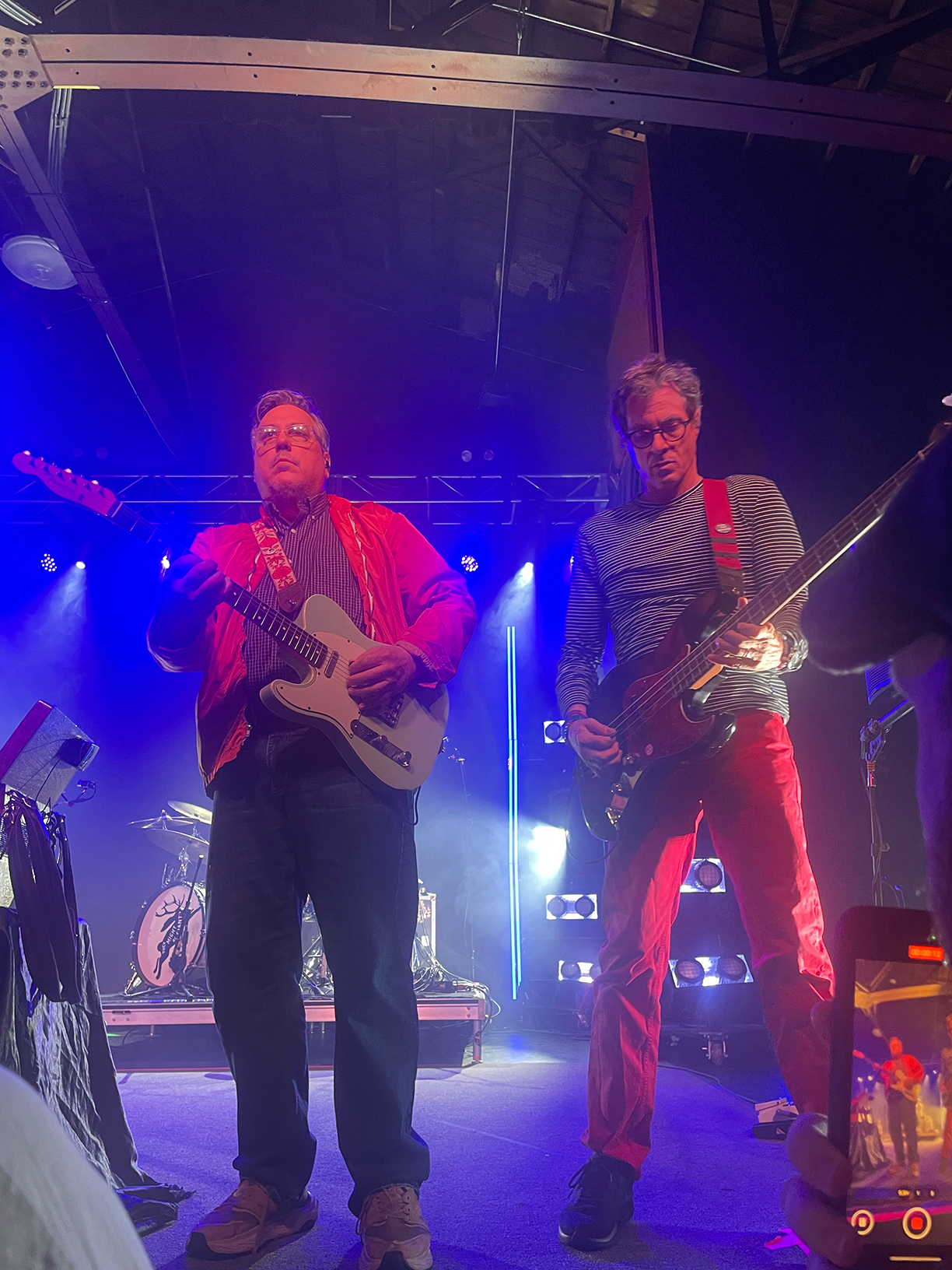 John Flansburgh and Danny Weinkauf on stage. Flansburgh is playing guitar whilst Weinkauf is playing bass guitar.