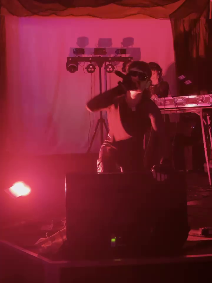 Ronnie Stone on stage. One member in the front singing into a microphone and another in the back behind a table working the electronics.