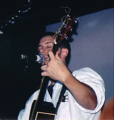 Burns playing his guitar and singing into a microphone.