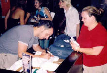 Burns at a table signing something for a fan.