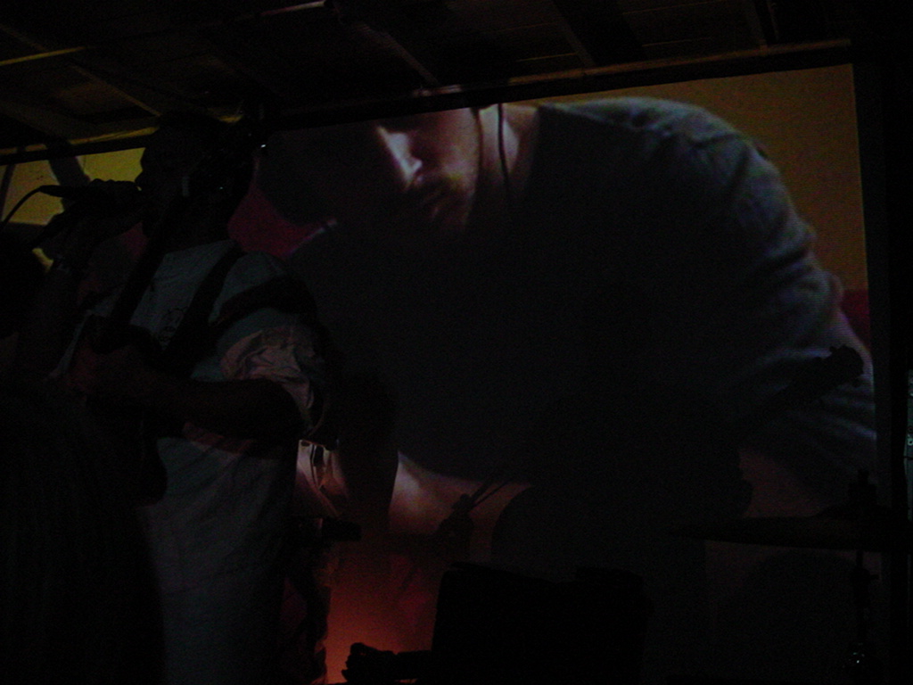 Burns performing on stage with projected video of him drumming the Thinking Chair.
