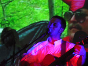 Burns performing on stage with video projected over him of a devil.