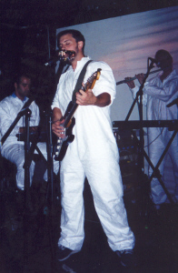 Burns playing on stage with his band behind him.