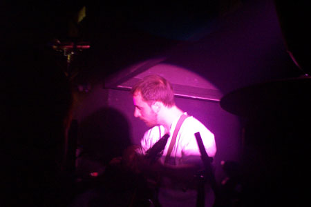 Burns playing on stage whilst a purple spotlight is on him.
