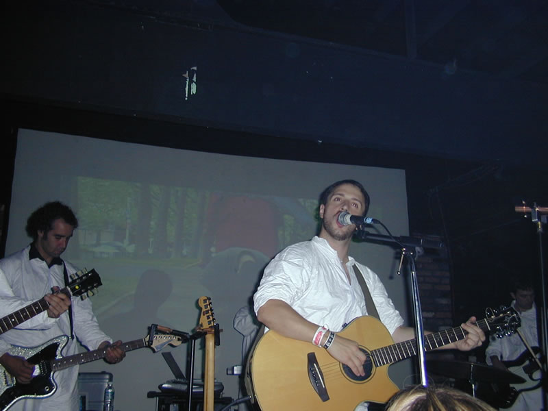 Burns singing whilst playing guitar. There are images projected behind him.