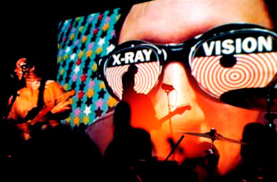 Burns performing on stage whilst an image of him wearing x-ray goggles is projected behind him.