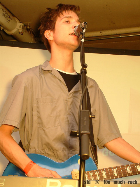 Derek playing guitar and singing into the microphone on stage.