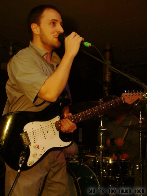 Burns playing electric guitar and singing into the microphone on stage.