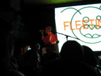 Burns on stage whilst an image of a dustmite with the word FLEETING over it is projected on the screen behind him.
