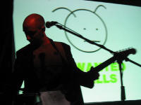 Burns performing on stage whilst a dustmite is being projected on the screen behind him.