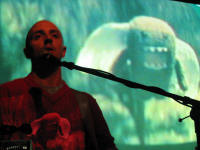 Burns performing whilst an image of Domo with wings is being projected on his shirt and on the screen behind him.