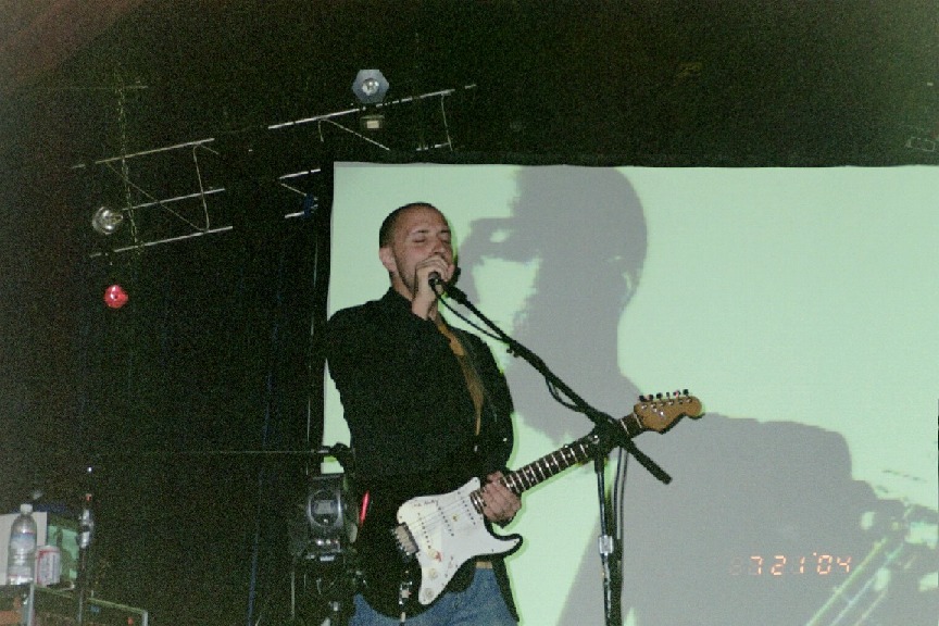 Burns performing on stage whilst an image of himself is being projected on the screen behind him.