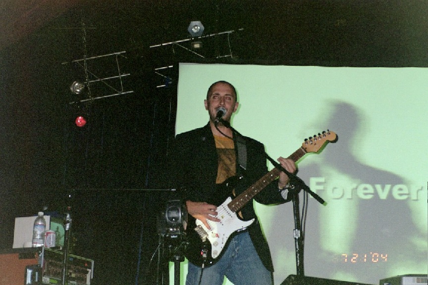 Burns performing on stage whilst an image of himself with the word Forever over him is being projected on the screen behind him.