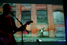 Burns on stage whilst an image of a man dancing in front of buildings is projected behind him.