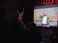 Burns jumping whilst a video plays behind him projected on the screen.