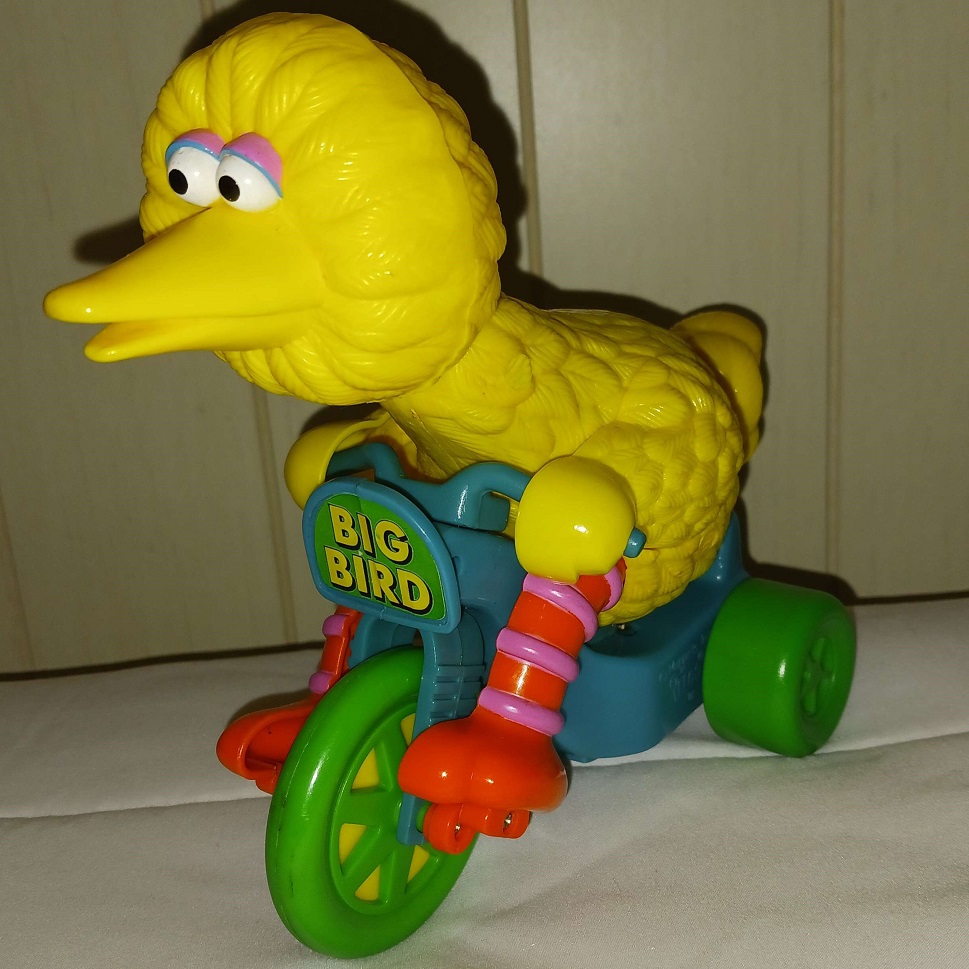 A plastic toy of Big Bird riding a tricycle.
