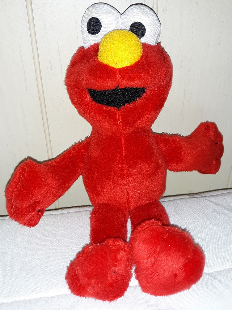 A plush doll of Elmo. His eyes are made of fabric and his mouth is open.