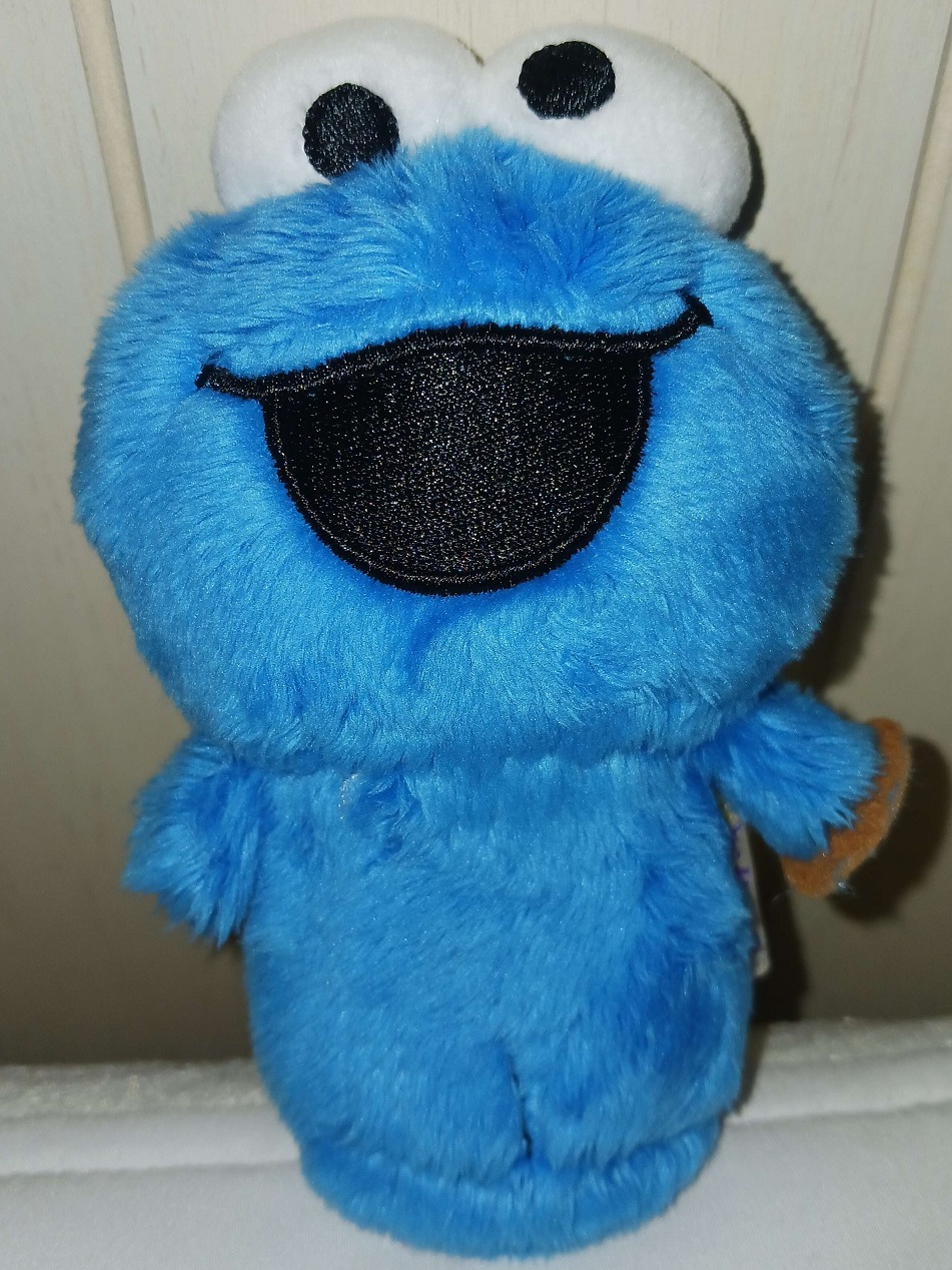 A miniature plush doll of Cookie Monster. He has fabric eyes with an embroidered smile. His arms are short and stubby and he has no legs. One arm is holding a cookie.