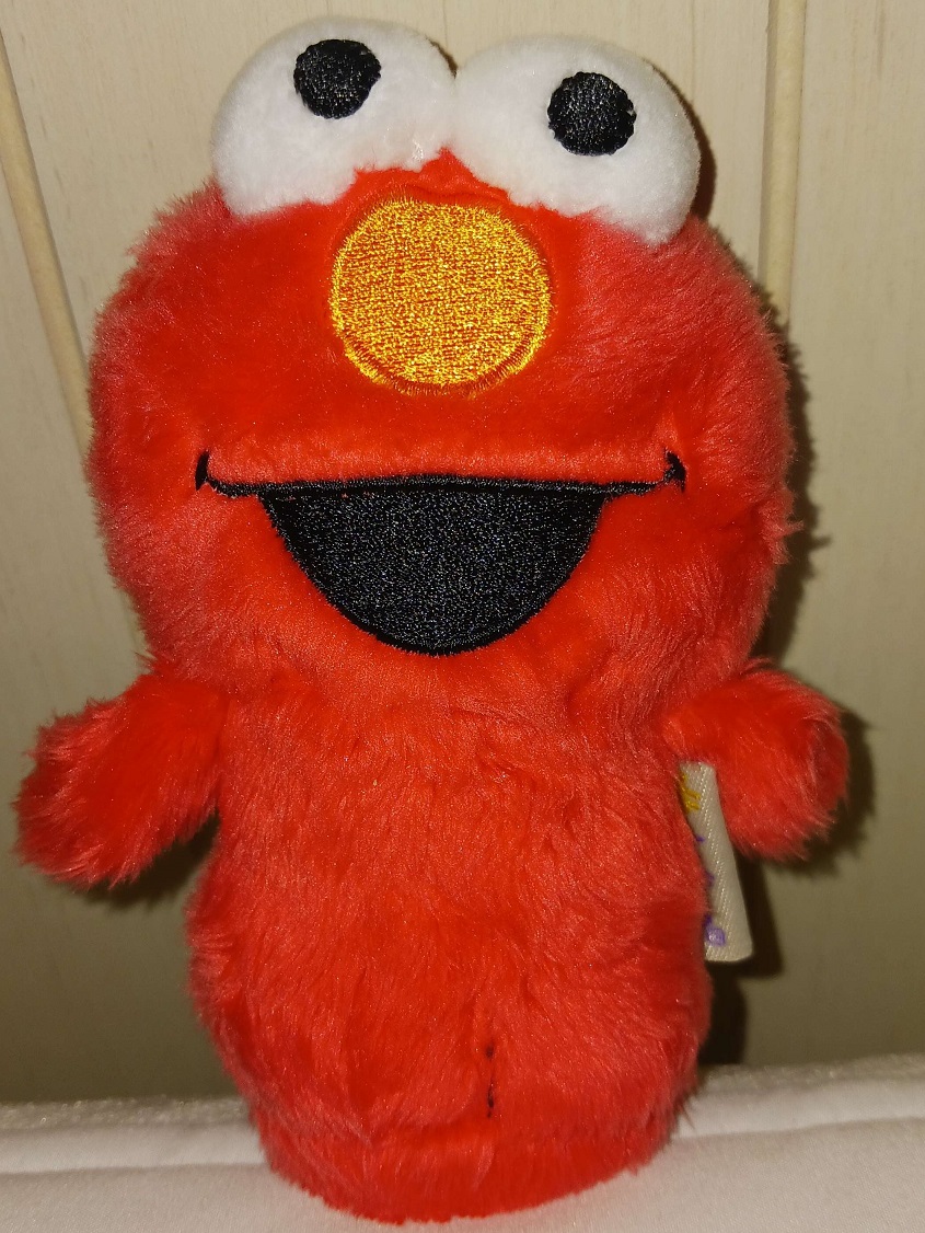 A miniature plush doll of Elmo that has fabric eyes and an embroidered on smile. His arms are stubby and he lacks legs.