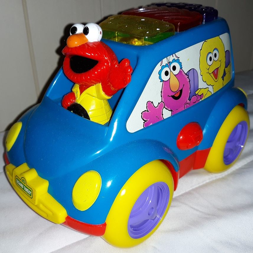 A plastic toy of Elmo driving a blue car with his friends printed on the sides of it. There are buttons on the top that light up.
