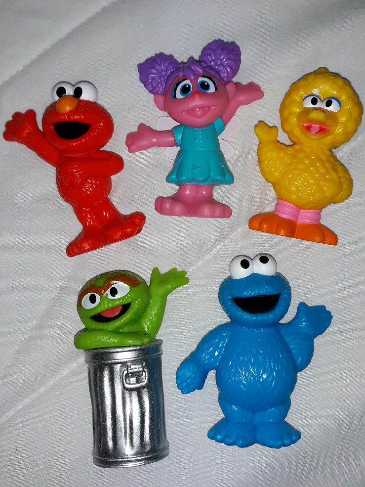 A group of plastic Sesame Street figurines consisting of Elmo, Abby, Big Bird, Oscar, and Cooking Monster.