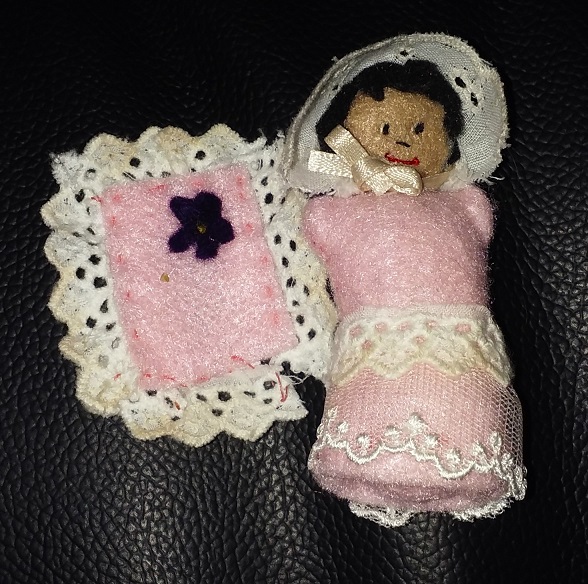 A tiny baby doll with a bonnet and a pink onesie. She also has a pink blanket with her.