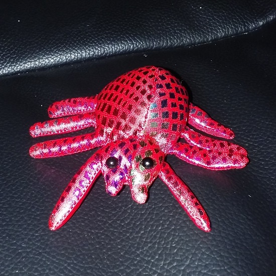 A red spider doll with holographic squares on it and two black bead eyes.