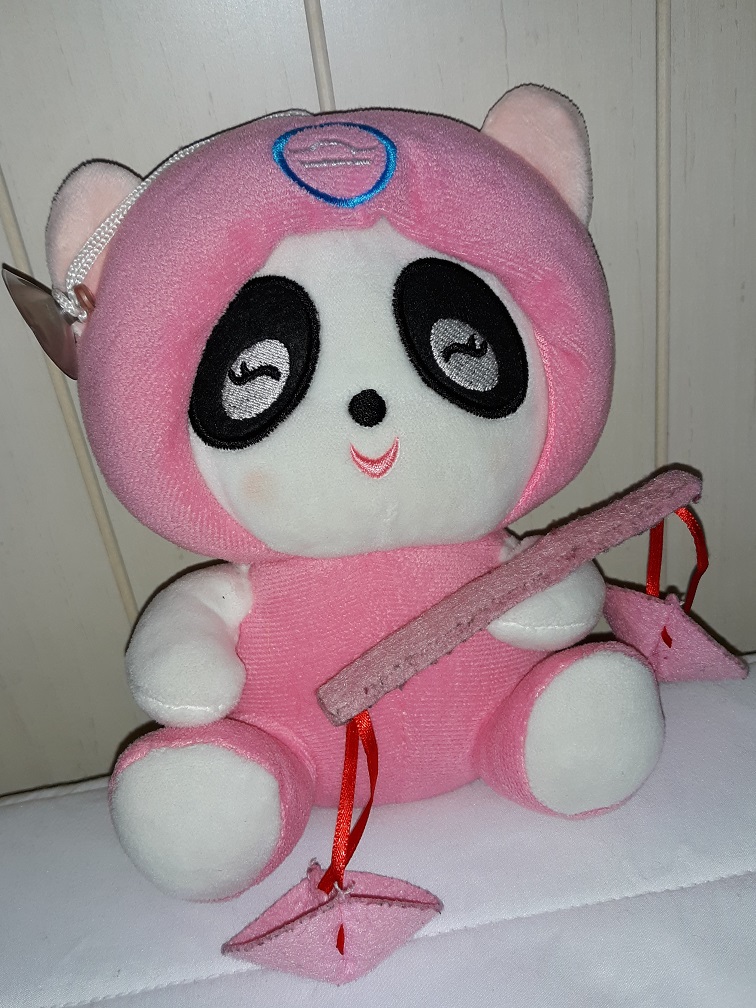 A plush panda wearing a pink and white onesie. She has a pink scale in one hand representing the horoscope Libra.