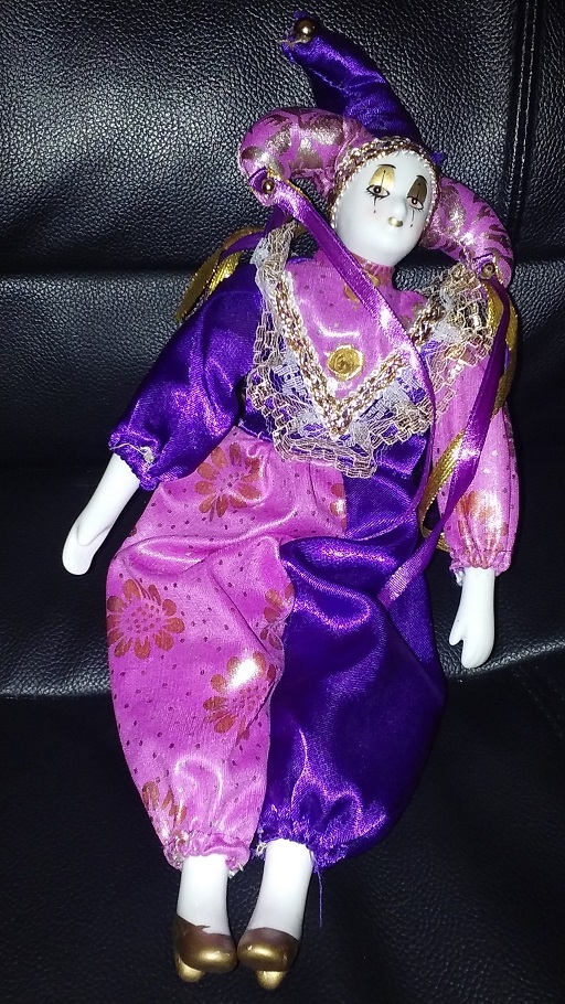 A purple and pink clothed white porcelain jester with gold makeup and shoes.