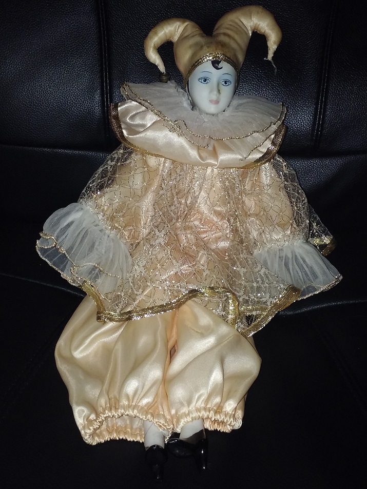 A light yellow clothed white porcelain jester with blue makeup and black shoes.