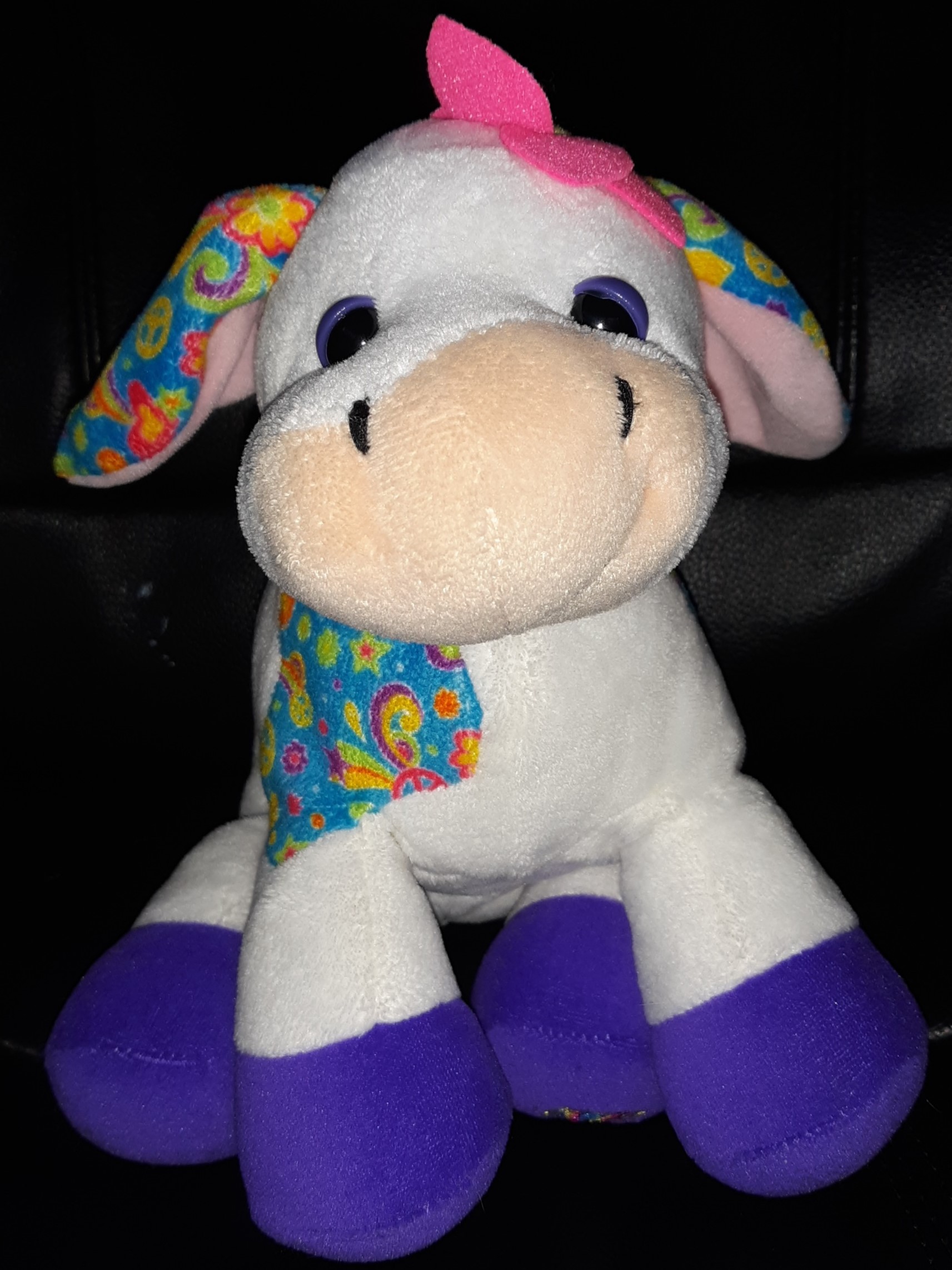 A doll of a white cow with purple hooves and patches of blue with a colorful pattern.